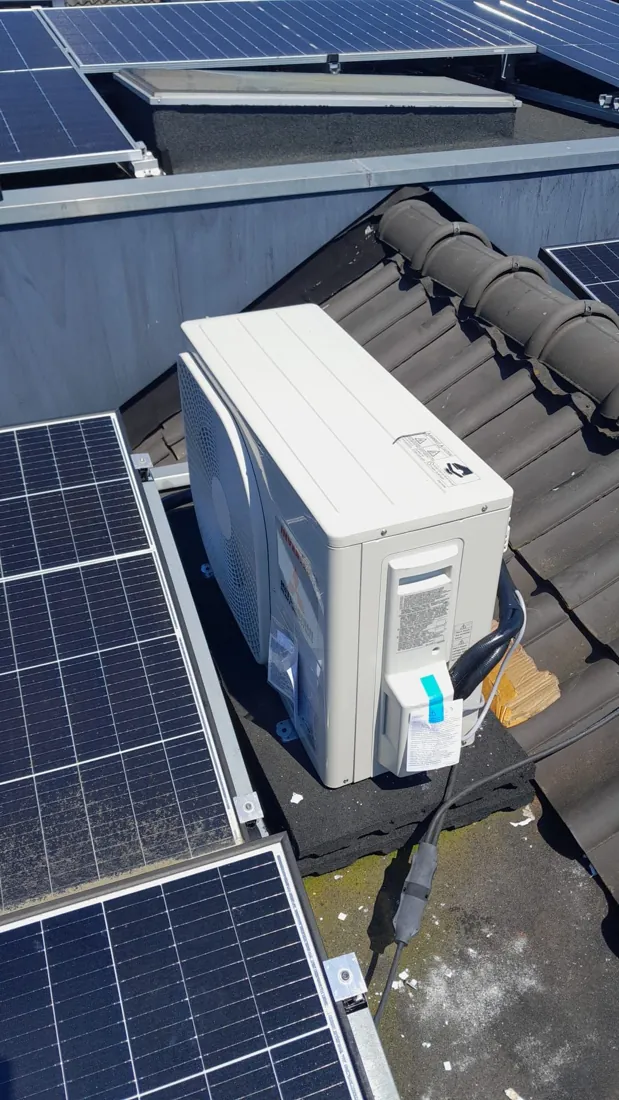 Airco-buitenunit geïnstalleerd tussen zonnepanelen op een schuin dak